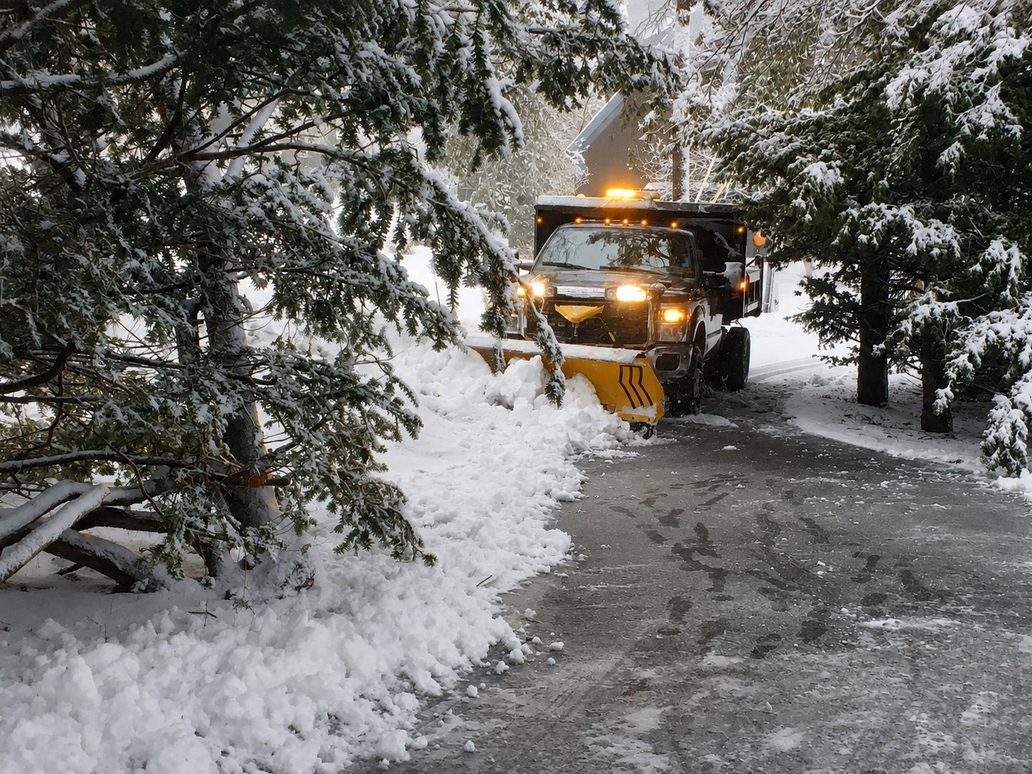 Truck plowing a snow-covered driveway with plow lights on