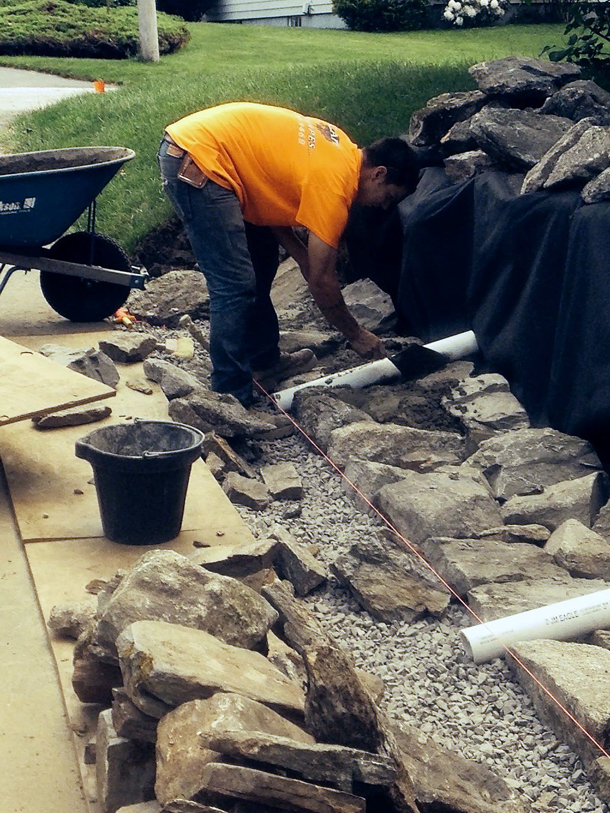 Crew setting drainage stone and pipe behind a wall before backfill