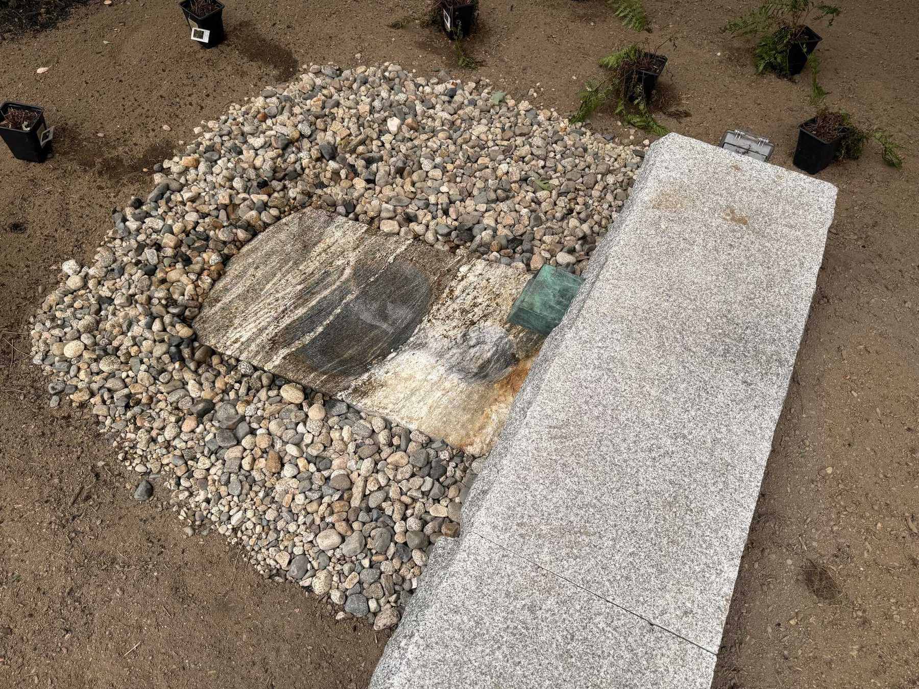 The fountain at the end of the granite retaining wall, with the water outlet set into a river-rock bed