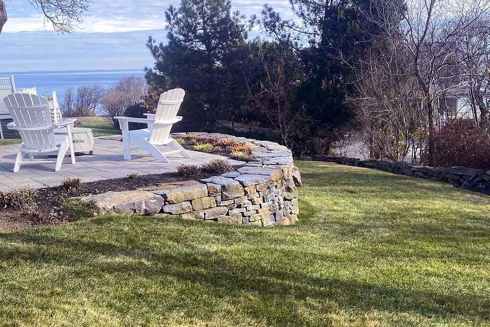 Curved stone terrace with two white Adirondack chairs overlooking the lawn