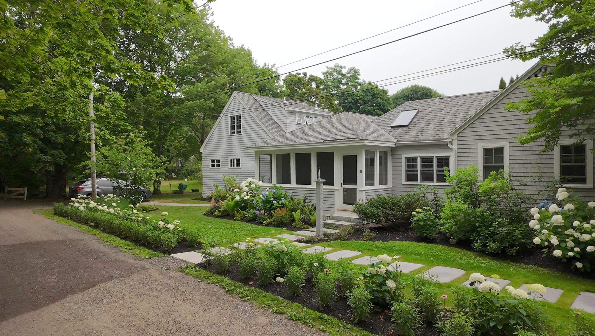 Aerial front view of the house with hydrangeas in bloom along the front walkway and a stepping stone path to the door