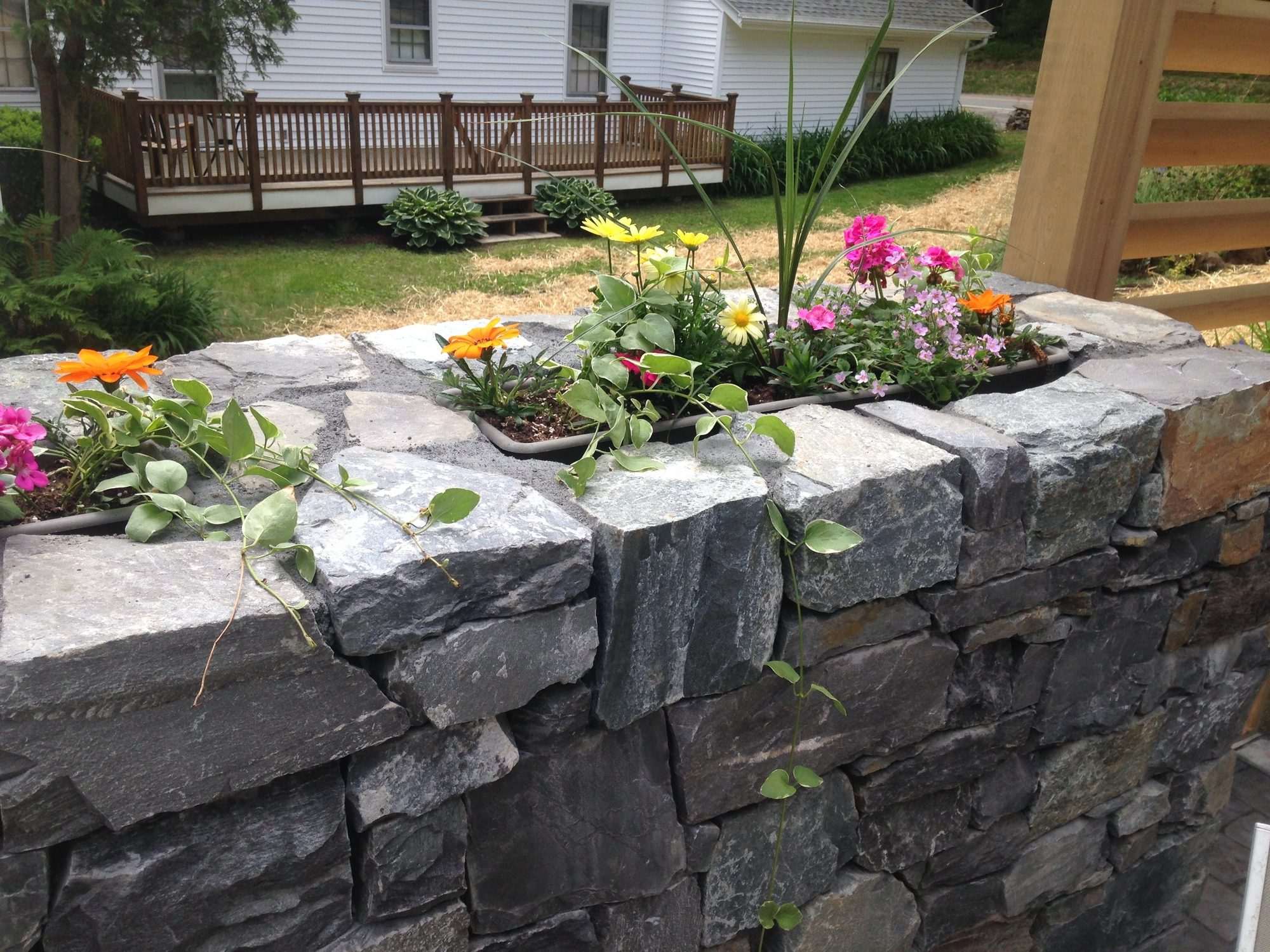 Stone wall with a flowering planter box and deck beyond