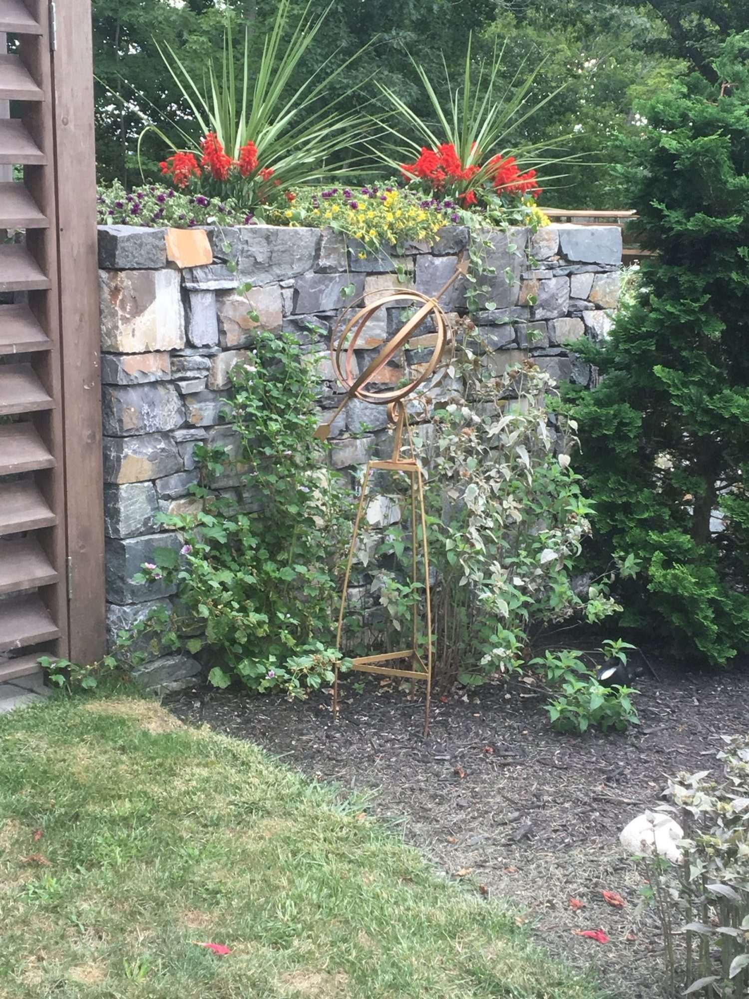 Stone wall with garden sculpture and red flowers