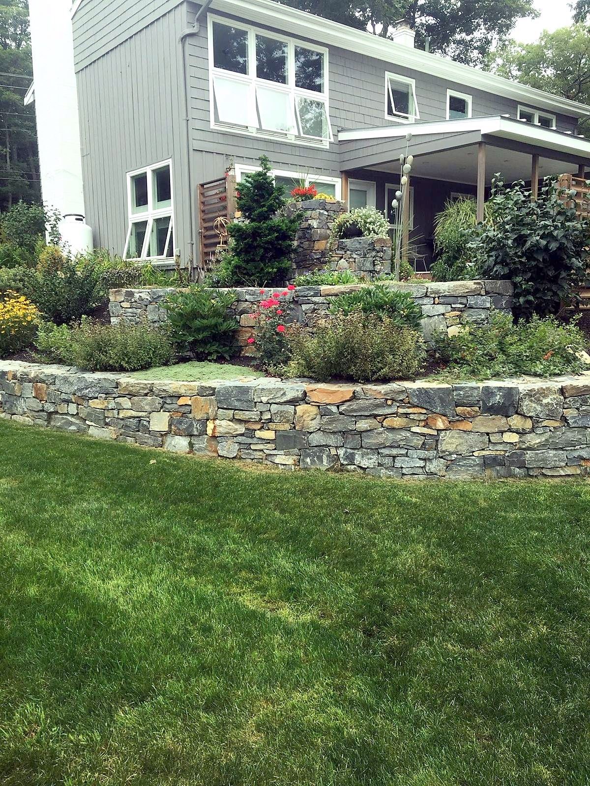 Tiered stone retaining walls with garden beds below the house