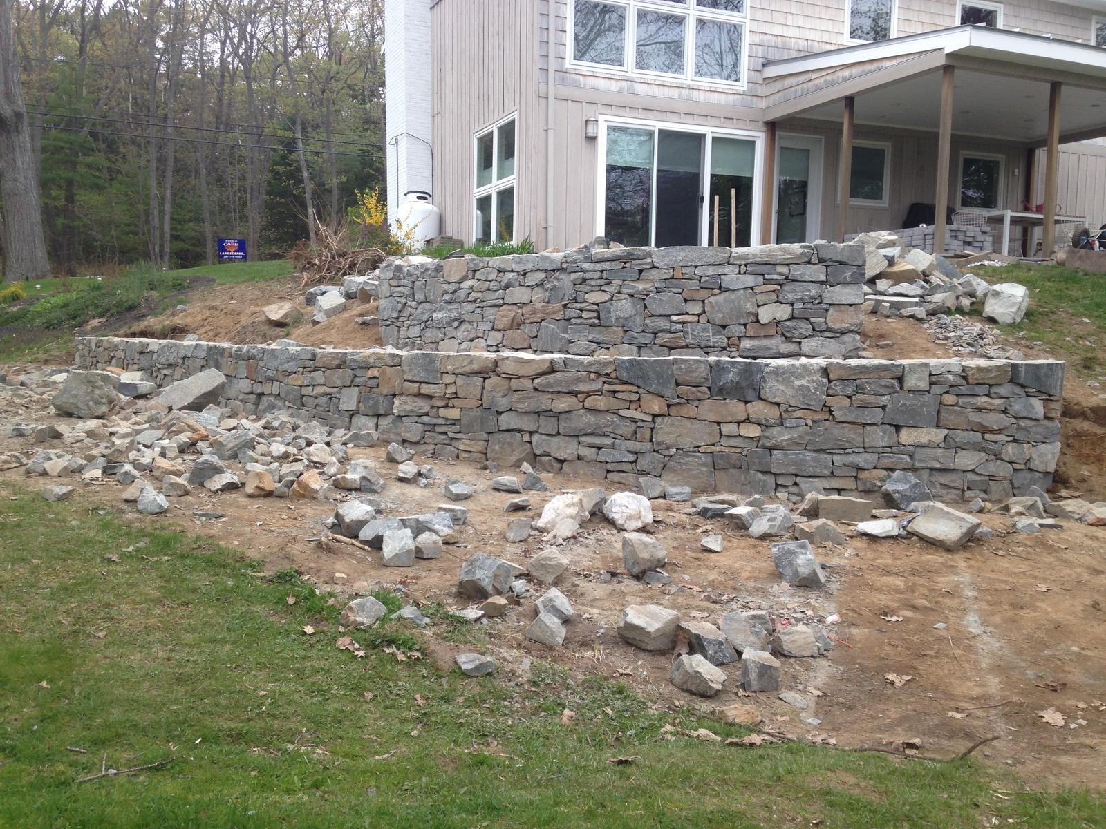 Curved retaining wall under construction with stone piled nearby