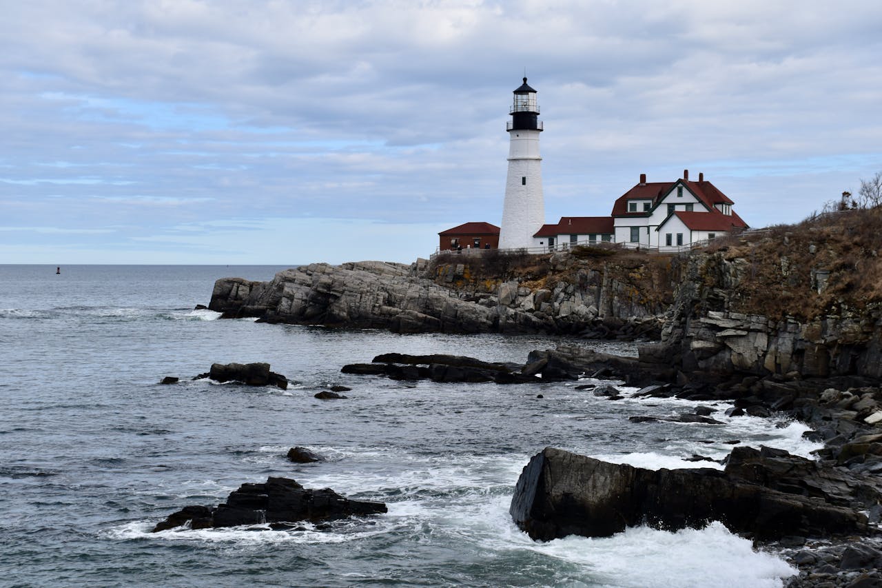 Portland Head Light in Maine overlooks a dramatic rocky coast and ocean under a cloudy sky, perfect for serene seascape views.